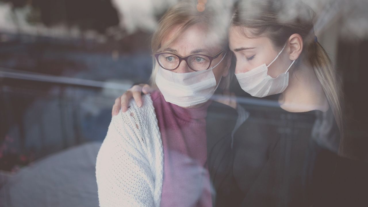 A mother and daughter experiencing declining mental health are holding one another while gazing out a window.