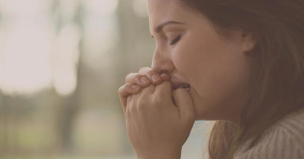 A woman who struggles to talk about feelings cries while sitting near a window.