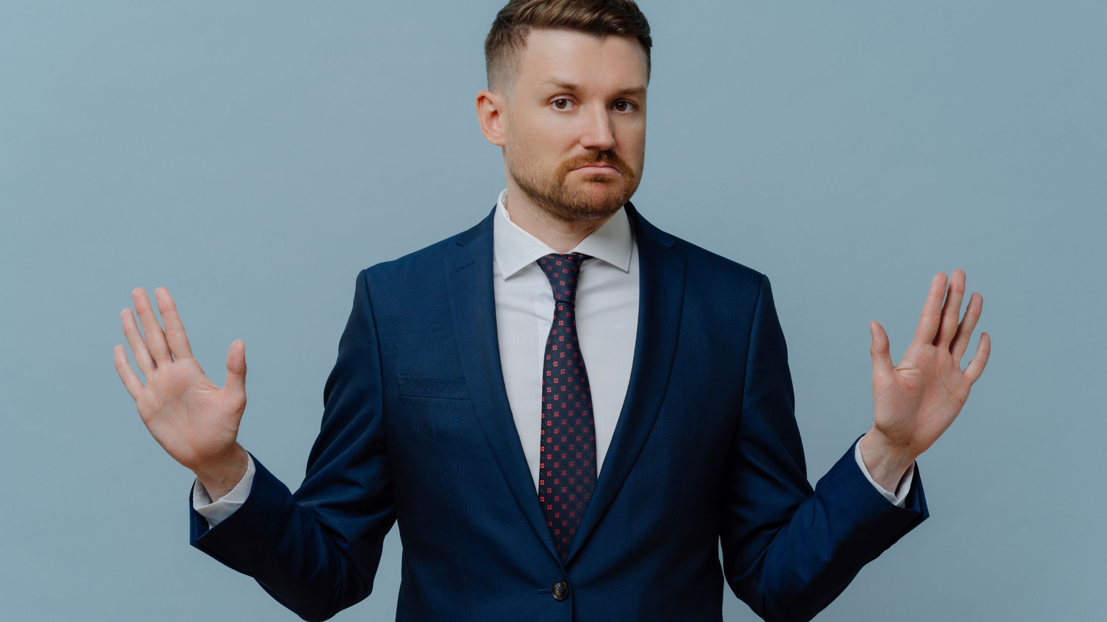 A manager in a blue suit and tie raises his hands in defeat, while avoiding conflict in the workplace.