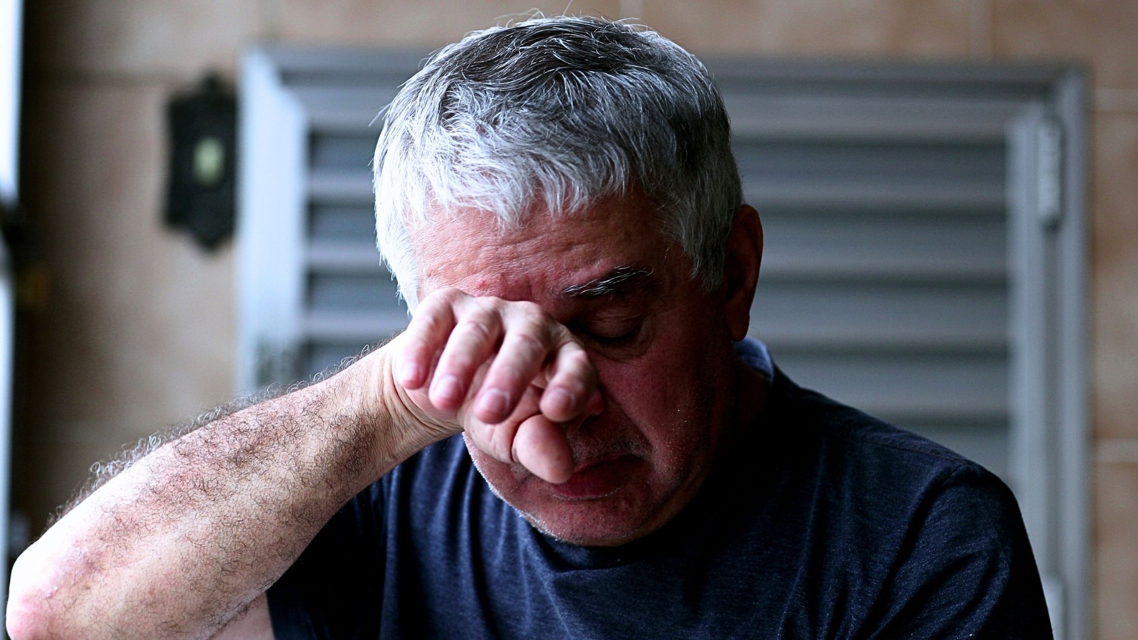 A middle aged man with silver hair rubs his eyes after crying, representing prolonged grief disorder.