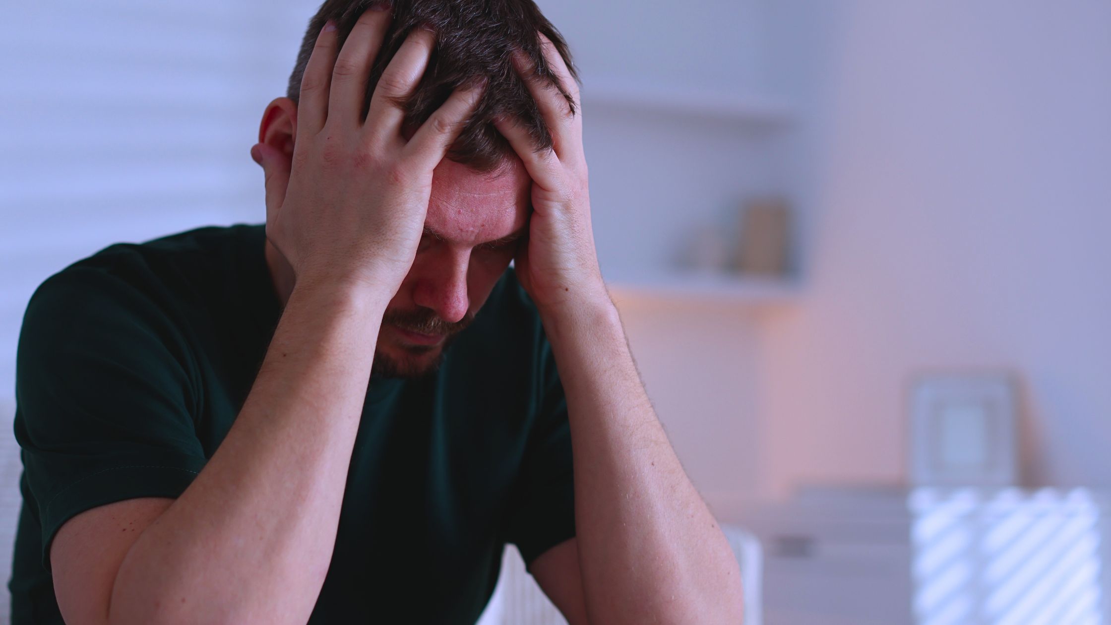 A man cradles his head in his hands while experiencing overwhelming anxiety as a result of the OCD cycle.
